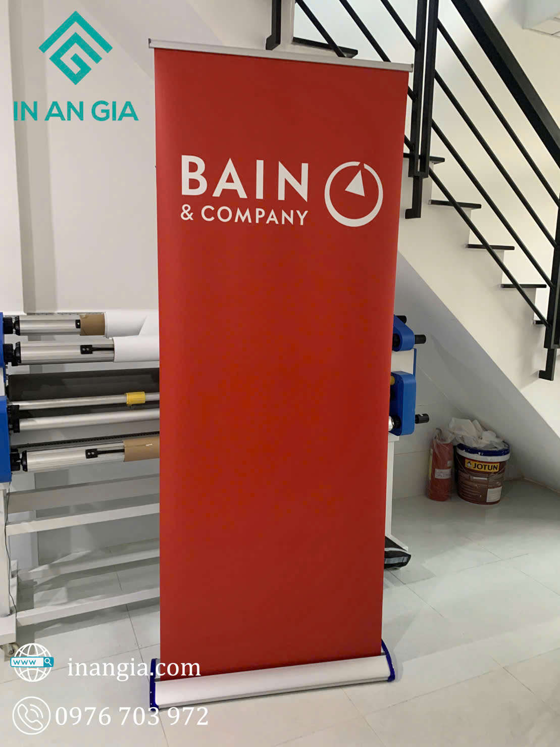 Standee cuốn nền đỏ in logo Bain & Company đặt trong xưởng in An Gia