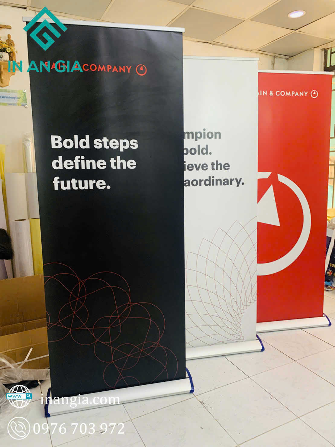 Ba standee quảng cáo Bain and Company màu đen trắng đỏ in slogan và họa tiết, đặt trong phòng in ấn
