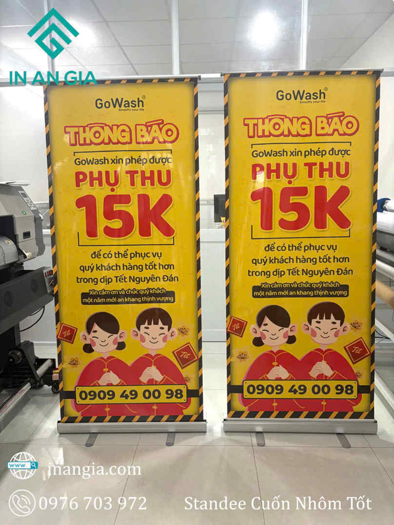 Standee cuốn nhôm GoWash màu vàng thông báo phụ thu 15K dịp Tết với hình minh họa bé trai bé gái